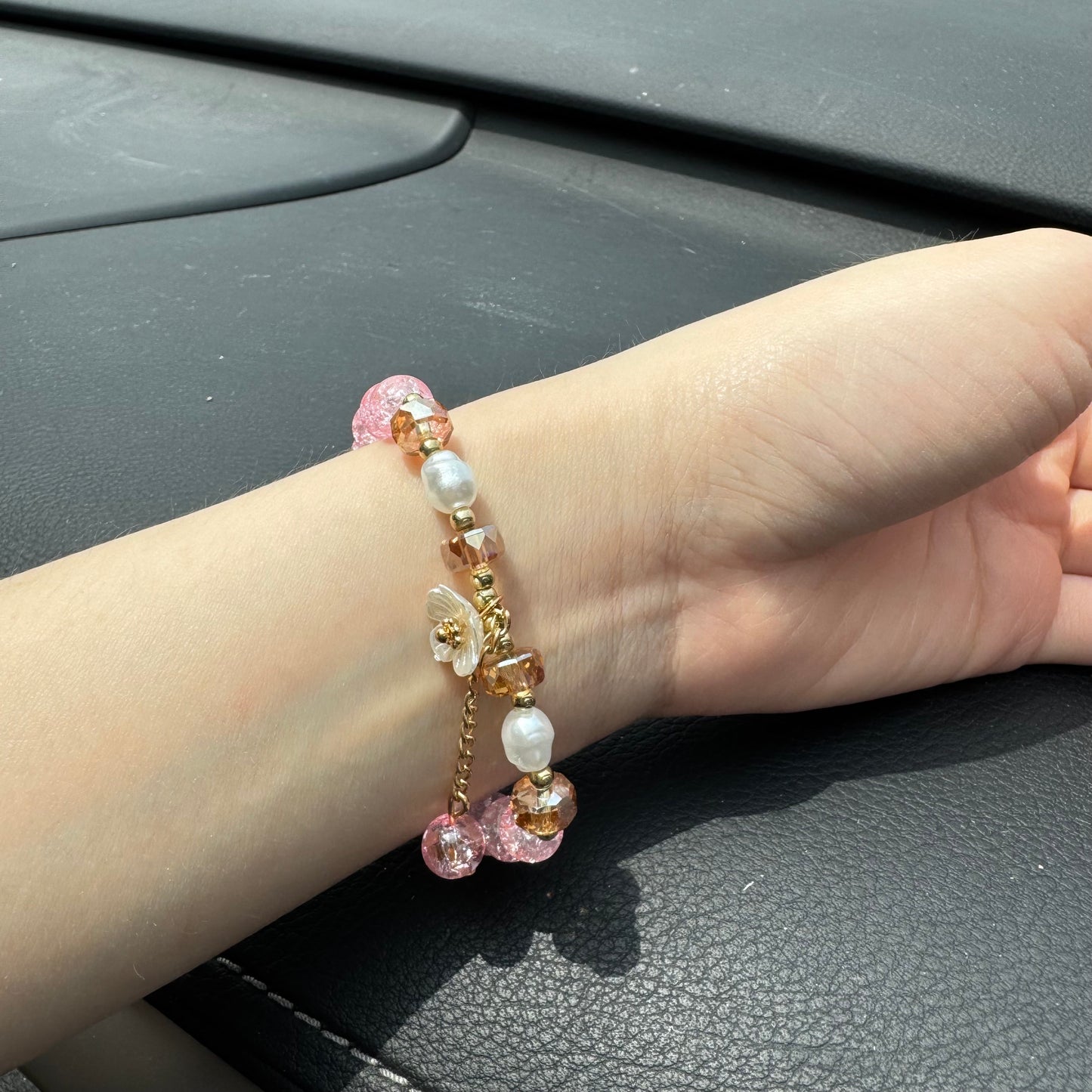 Handmade pink crackle beaded bracelet with white flower charm, gold crystals, and dangling bead, displayed in a gift box