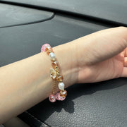 Handmade pink crackle beaded bracelet with white flower charm, gold crystals, and dangling bead, displayed in a gift box