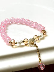 Handmade pink crackle beaded bracelet with white flower charm, gold crystals, and dangling bead, displayed in a gift box
